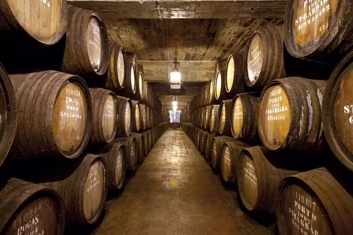 Explore the historic wine cellars of Porto on a private tour from Lisbon, featuring rows of aging barrels in a rustic setting.