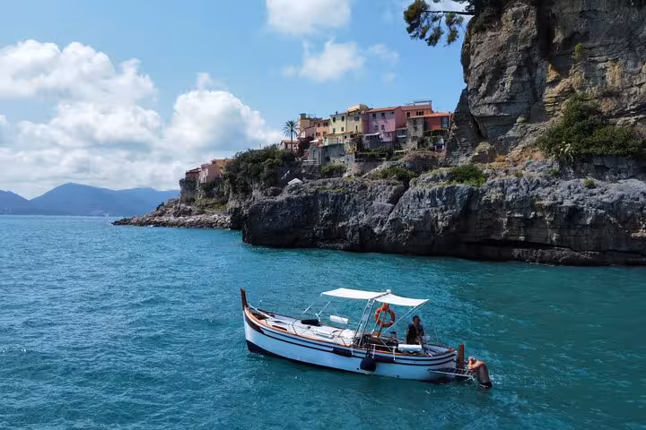 Small boat near rocky cliffs and colorful houses in Portovenere, Italy.