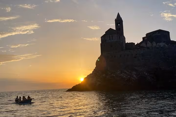 Silhouette of a historic building at sunset with a small boat passing by in the waters near Portovenere.