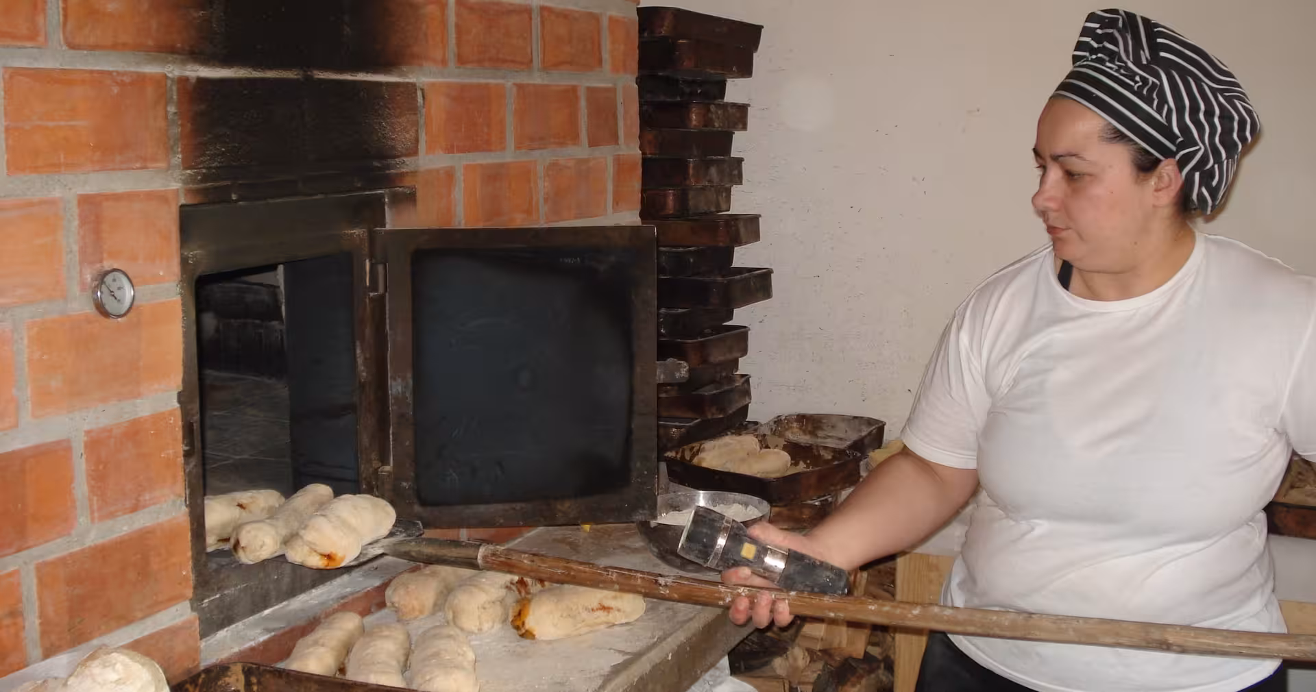 Baker pulls fresh bread from a traditional oven during Portugal cooking class on 8-day food and wine tour