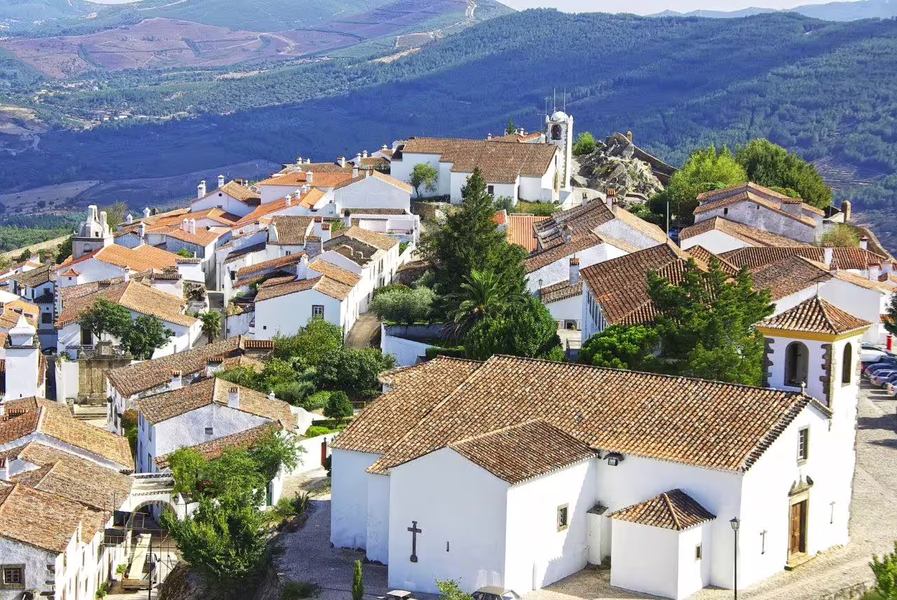 Scenic view of a picturesque Portuguese village with whitewashed houses and terracotta roofs nestled in lush green hills.