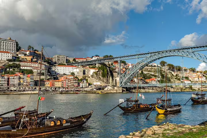 Traditional boats on Douro River with scenic view of Porto and Dom Luís I Bridge, perfect for Portugal tour from Lisbon.
