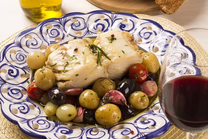 Elegant plate of Portuguese bacalhau with potatoes and olives, accompanied by red wine, ideal for Lisbon food tour.