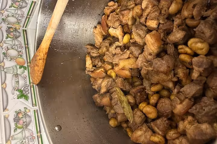 Close-up of a traditional Portuguese dish with meat and chestnuts simmering in a pot during a cooking class.