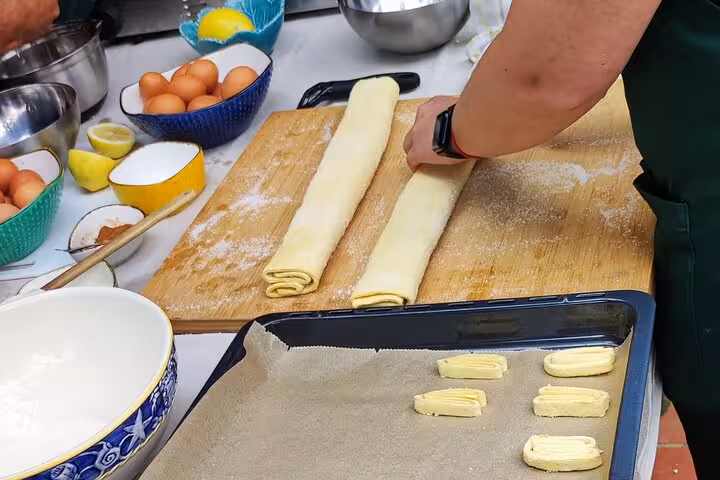 Hands preparing traditional Portuguese pastry dough on a wooden board during a cooking class on a scenic terrace.