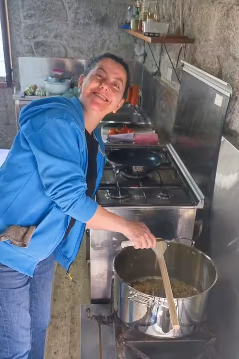 Chef stirring a pot on a terrace during a Portuguese cuisine cooking class, smiling and engaging with participants.