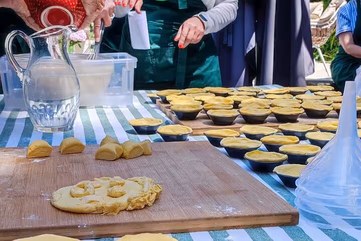 Participants prepare traditional Portuguese pastries on a sunlit terrace during a hands-on cooking class.