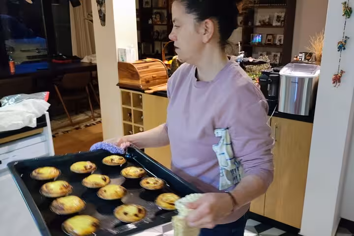 Woman holds a tray of freshly baked Portuguese tarts during a cooking class on a scenic terrace.