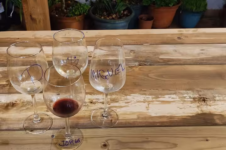 Four wine glasses labeled with names on a rustic wooden table, set on a terrace for a Portuguese cooking class.