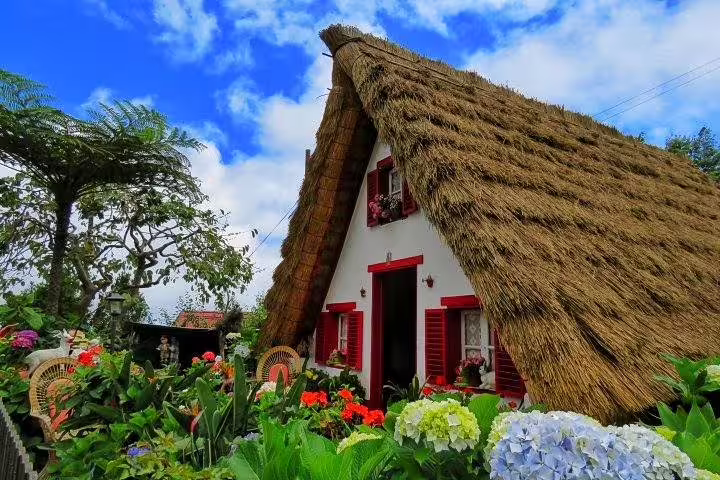 Charming traditional Portuguese thatched cottage surrounded by vibrant flowers, perfect for cultural exploration tours.