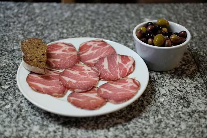 A plate of traditional Portuguese cured meats with rustic bread and a bowl of mixed olives on a granite countertop.