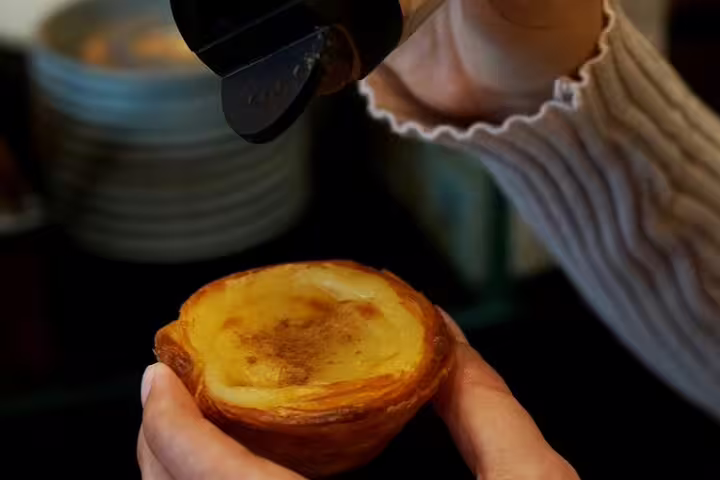 Hand sprinkling cinnamon on a traditional Portuguese custard tart during a food and walking tour.
