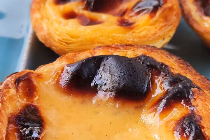 Close-up of freshly baked Portuguese custard tarts with golden, flaky crusts from a terrace cooking class.
