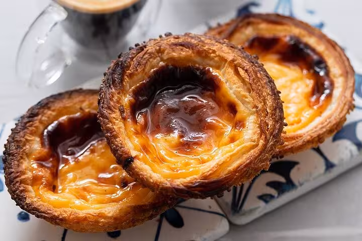 Traditional Portuguese pastéis de nata pastries with a crispy crust and creamy filling, paired with coffee.