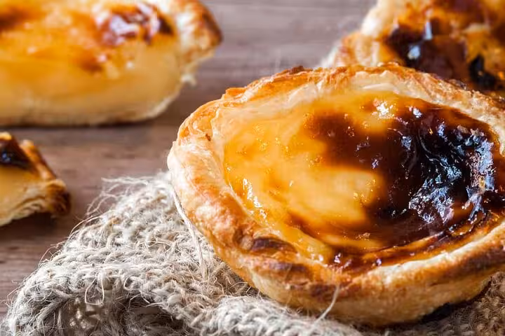 Close-up of traditional Portuguese Pastel de Nata pastries on a rustic burlap cloth, highlighting Lisbon's iconic dessert.