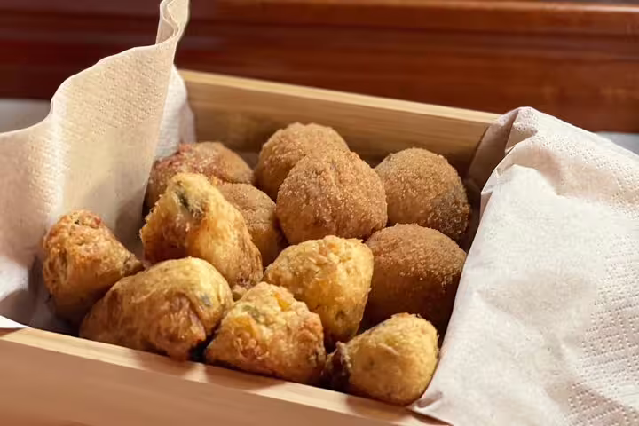 A wooden box filled with freshly fried Portuguese pastries, offering a taste of Madeira's culinary delights on a sailing tour.