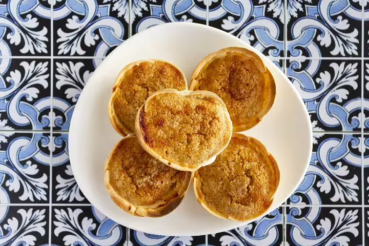 A plate of traditional Portuguese queijadas on a decorative tile background, featured in the Sintra Highlights and Pena Palace Tour.