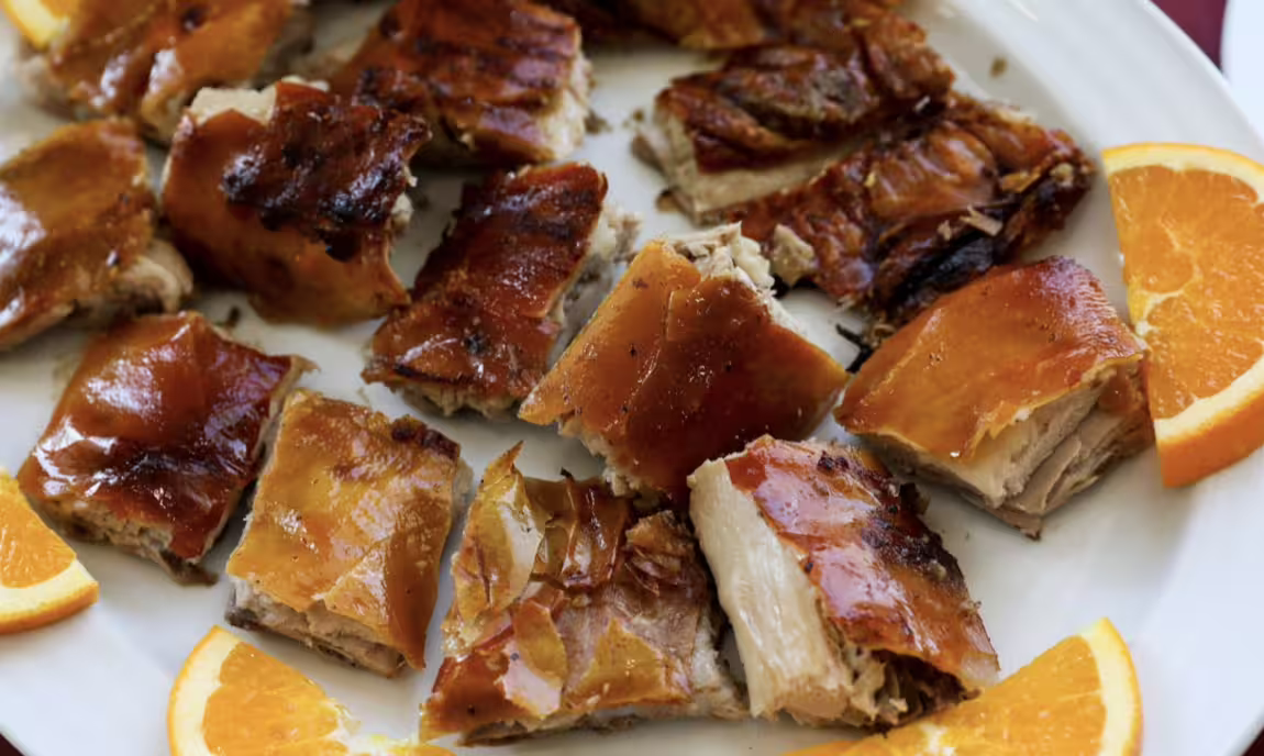 Savor traditional Portuguese roasted piglet with citrus slices on a Lisbon to Porto day trip.