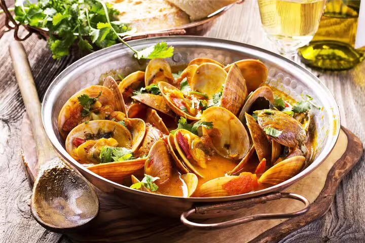 Portuguese seafood stew in a rustic pan with fresh herbs, highlighting local cuisine on the Sintra, Cascais & Estoril private tour.