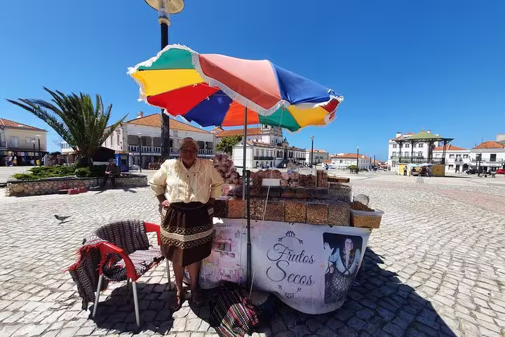 Local vendor selling traditional Portuguese snacks under a colorful umbrella in a scenic square on the Fátima, Nazaré, Batalha, and Óbidos tour.