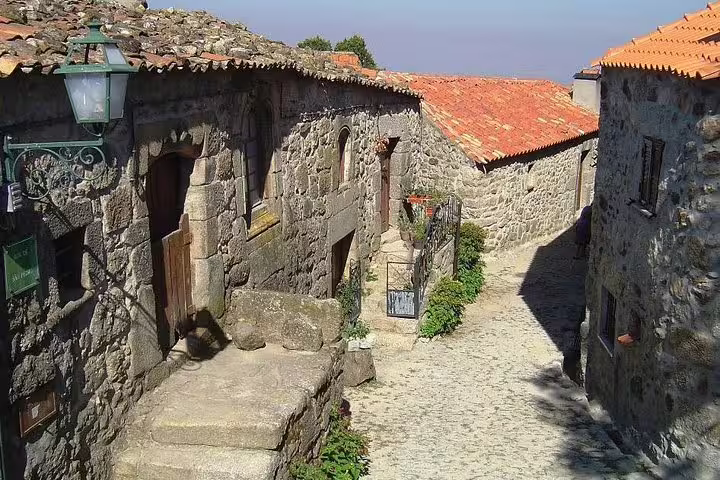 Charming cobblestone street in a Portuguese historical village with rustic stone houses and vibrant red roofs.