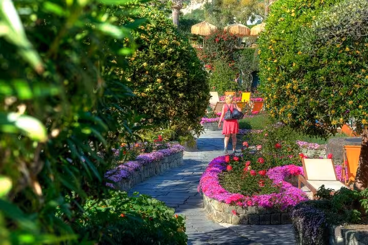 Visitor strolling through picturesque floral walkway in Poseidon Gardens, Ischia, surrounded by colorful blooms.