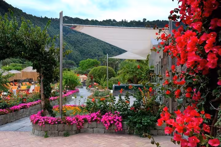 Lush garden path in Poseidon Gardens, Ischia, adorned with vibrant flowers and scenic mountain backdrop.