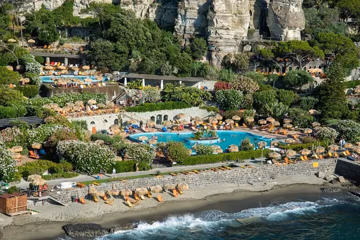 Scenic view of Poseidon Gardens nestled in cliffs with vibrant pools, lush greenery, and beach access in Ischia.