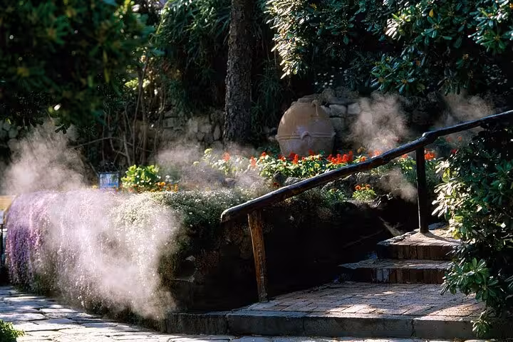 Steam rises from thermal springs in Poseidon Gardens, Ischia, amidst lush greenery and vibrant flower beds.