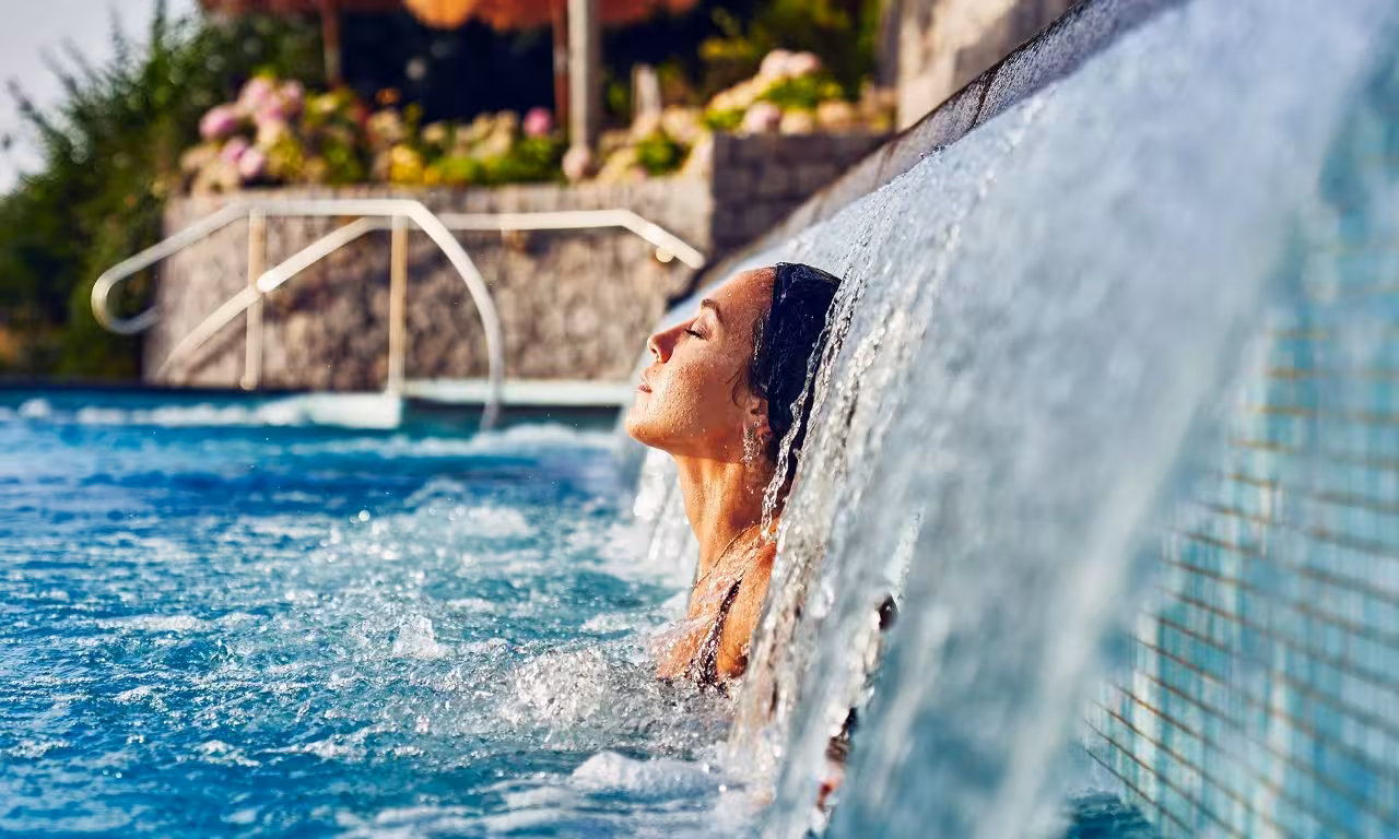 Guest relaxing under waterfall in Poseidon Gardens thermal pool, Ischia, with ticket and hotel transfer included