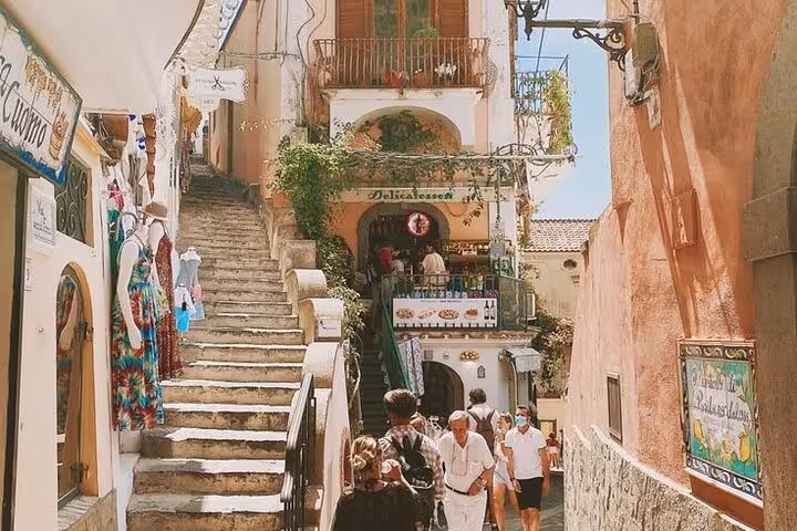 Charming Positano alleyway with vibrant shops and tourists exploring on a sunny day during a private tour from Naples.