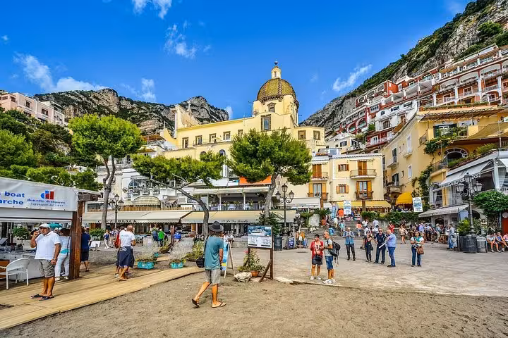 Bustling beachside promenade in Positano with vibrant shops and the iconic dome of Santa Maria Assunta Church.