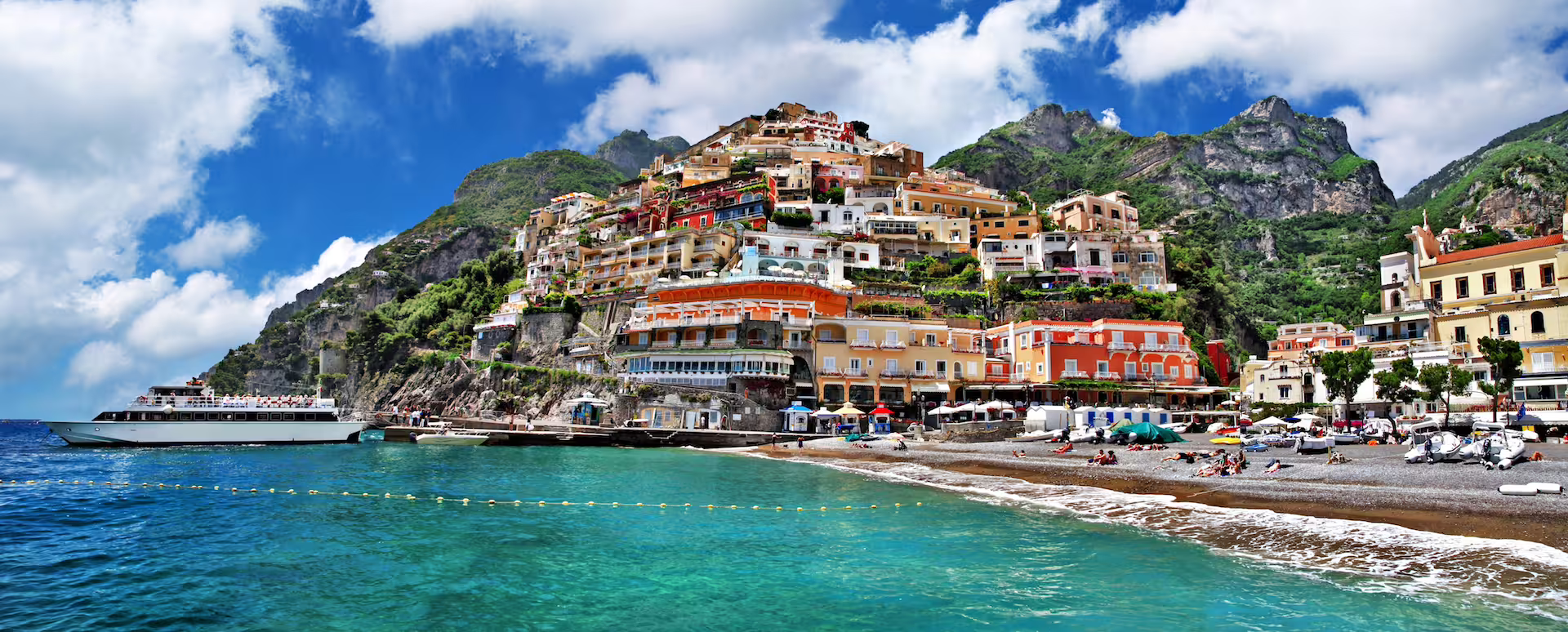 Scenic view of Positano's vibrant cliffside houses and a boat on the turquoise Amalfi Coast waters.
