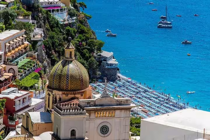 View over Positano’s colorful cliffside houses and church dome above a busy beach and turquoise sea on an Amalfi Coast day trip