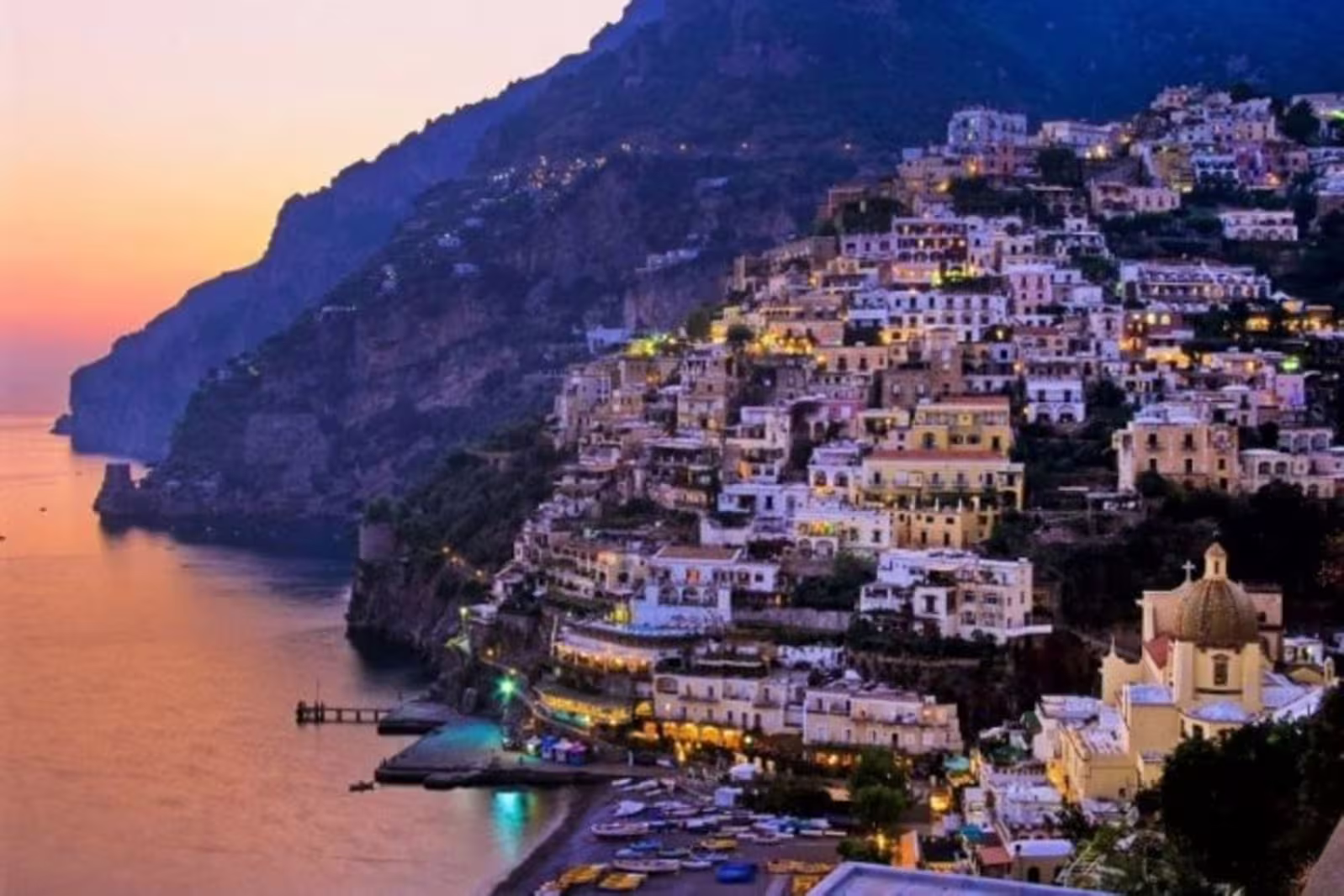 Positano at dusk with illuminated cliffside houses, church dome and tranquil Amalfi Coast shoreline on an evening tour