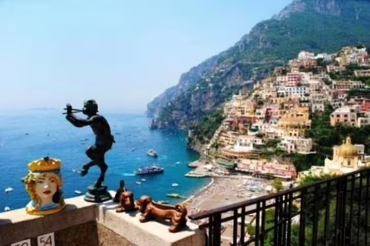 Iconic Positano skyline and beach from hilltop terrace with statues and boats on the sea, shared tour Ravello Amalfi Positano