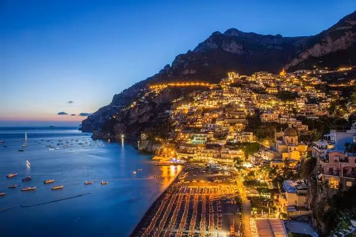 Scenic evening panorama of Positano's hillside lights reflecting on the sea, showcasing the beauty of the Amalfi Coast at dusk.