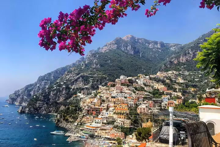 Breathtaking panorama of Positano's colorful cliffside buildings and azure sea framed by vibrant bougainvillea.