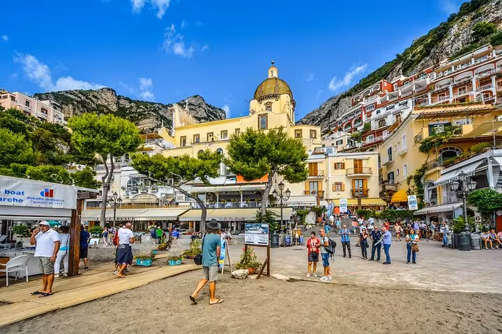 Bustling Positano beach scene with iconic dome church and vibrant hillside architecture on the Amalfi Coast tour.