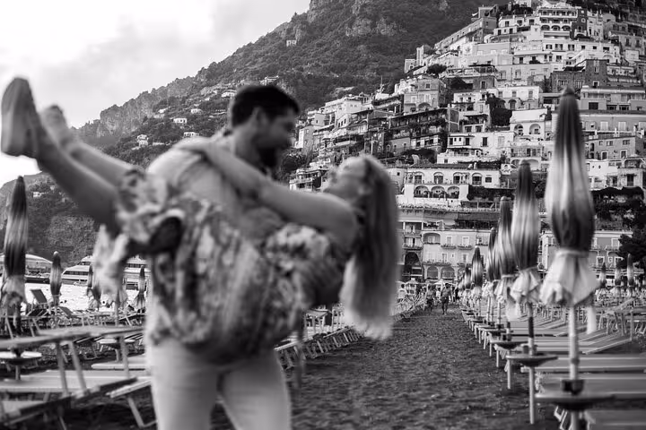 Romantic embrace on Positano sand with iconic cliffside backdrop, perfect moment captured in Amalfi Coast photography tour.