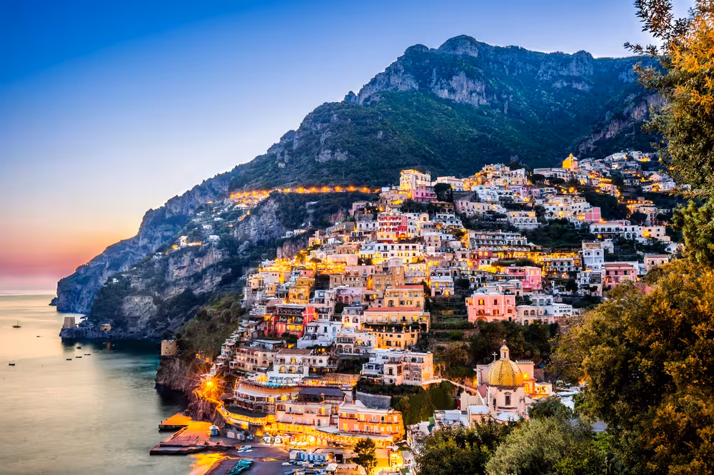 Scenic view of Positano at dusk with colorful buildings on the cliff, part of a Sorrento coast boat tour.