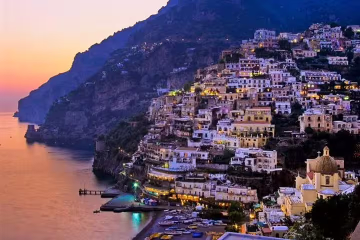 Sunset view of Positano on the Amalfi Coast with pastel houses on the cliff and boats in the bay, seen on a private tour