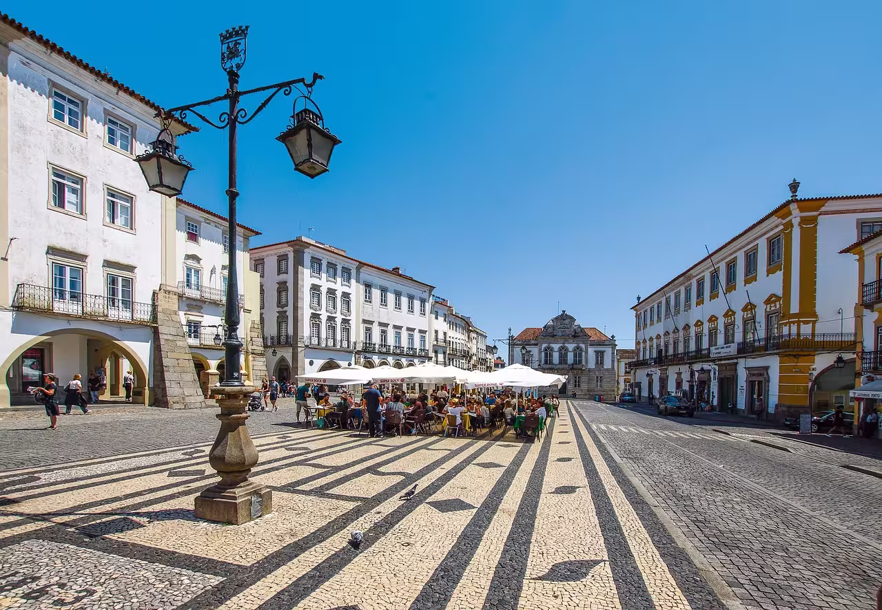Vibrant Praça do Giraldo in Évora with outdoor cafes, historic architecture, and sunny skies, perfect for Alentejo tours.