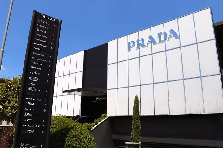Exterior of Prada store at The Mall with brand signage and directory of luxury labels under clear blue sky.