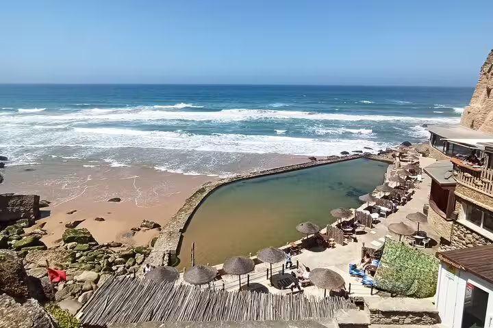 Scenic coastal view of Praia das Maçãs in Sintra with natural rock pools, beach umbrellas, and ocean waves.