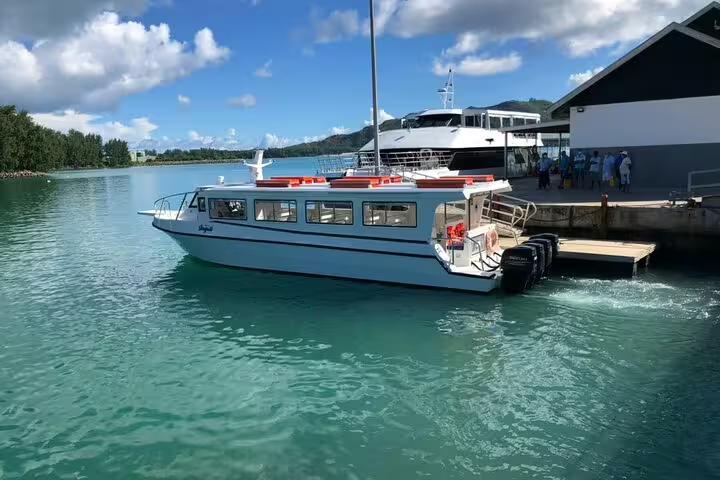 Scenic view of a ferry departing a dock, offering a shared day trip to Praslin and La Digue with clear blue waters.