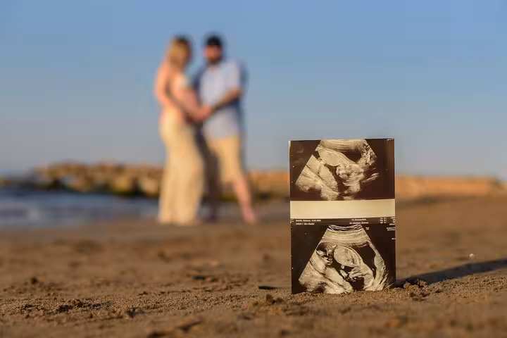 Ultrasound photo on sandy Heraklion beach with expectant couple in the background, symbolizing new beginnings.