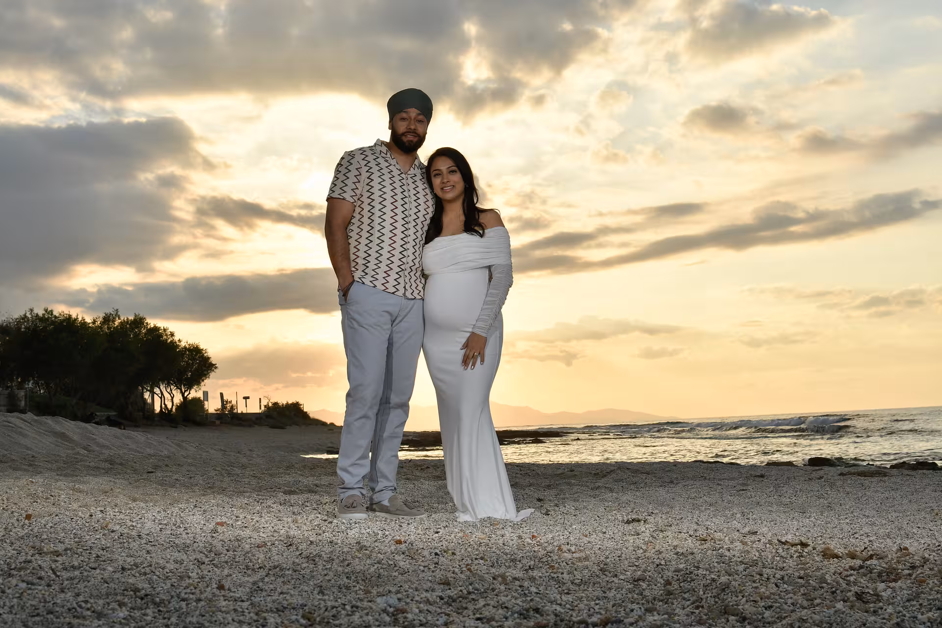 Pregnant couple posing on a picturesque Heraklion beach at sunset, ideal for a romantic photoshoot experience.