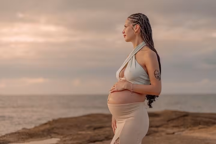 Pregnant woman embracing her belly on Ammoudara beach during a serene sunrise photoshoot.