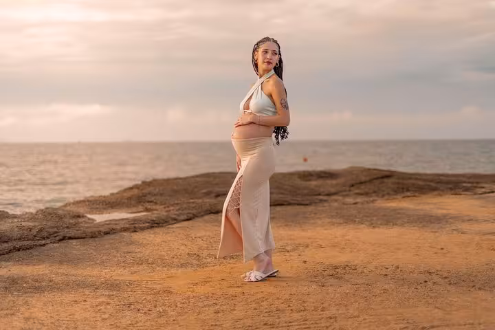 Pregnant woman posing gracefully by the rocky shore in Heraklion during a golden hour maternity photoshoot.